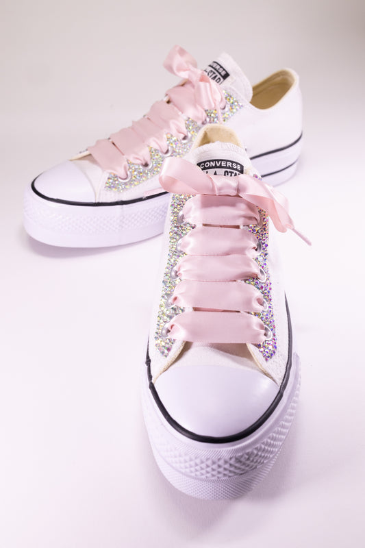 White Converse sneakers with pink laces and rhinestone embellishments on a white background